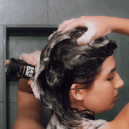 Shampoo bar lather on dark hair while squeezing product bottle