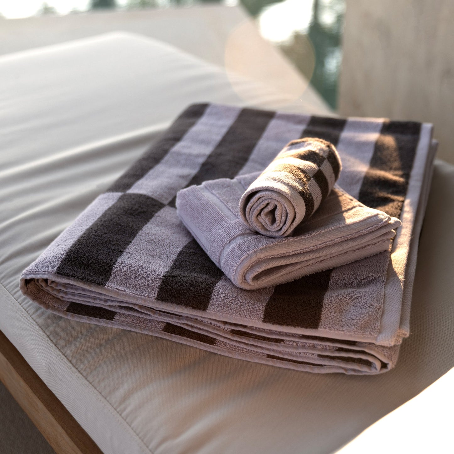 Rolled lilac and dark charcoal striped cotton towels on a surface