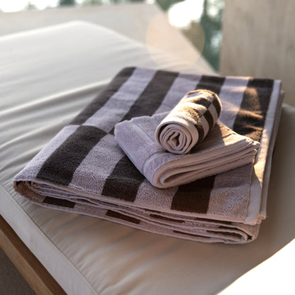Rolled lilac and dark charcoal striped cotton towels on a surface