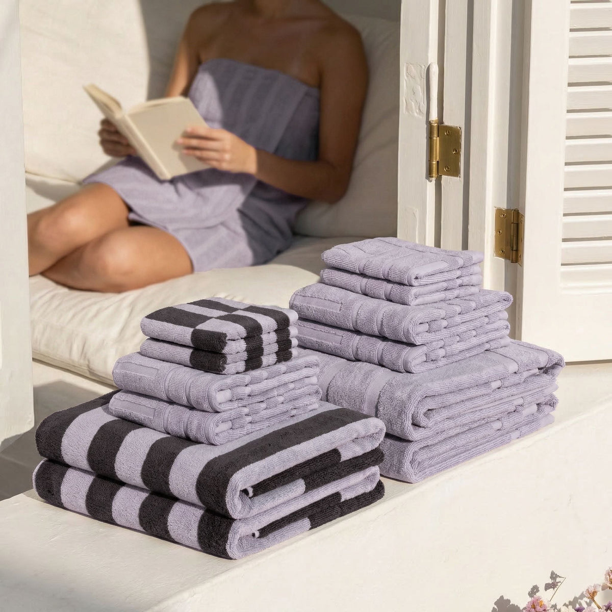 Lilac cotton towel set with black-and-white stripe accents, stacked on a bed