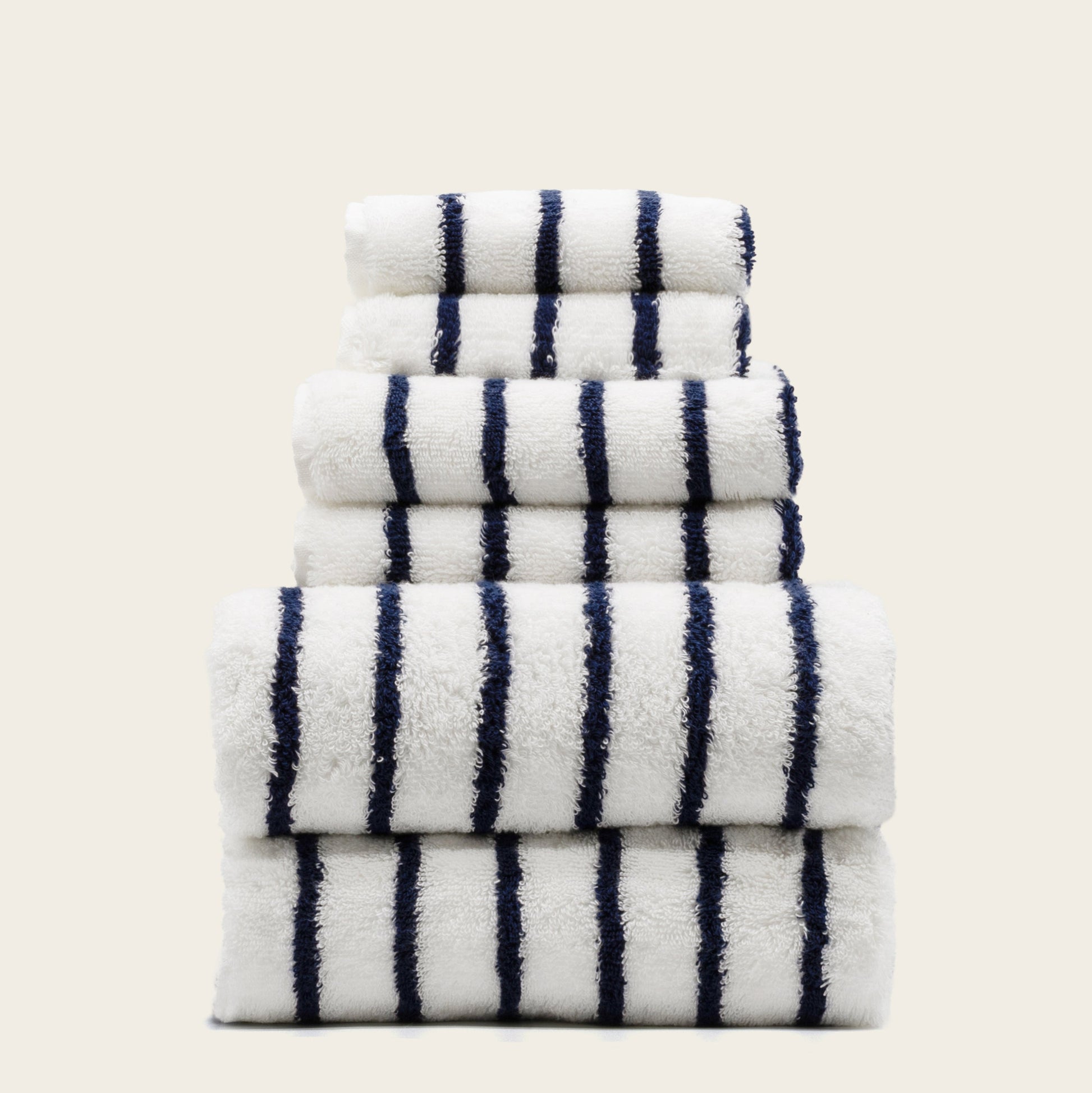 Stacked plush cotton towels, white with navy vertical stripe pattern, folded.