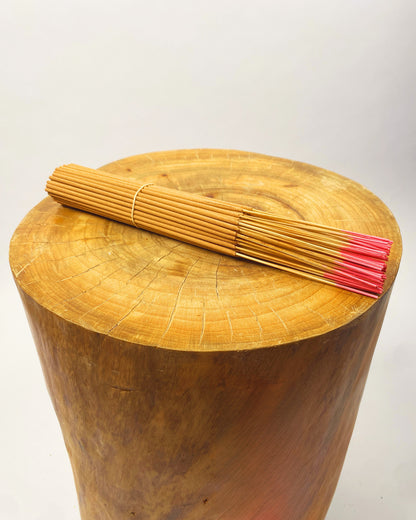 Incense sticks laid across wooden stump, tan bundle with pink ends