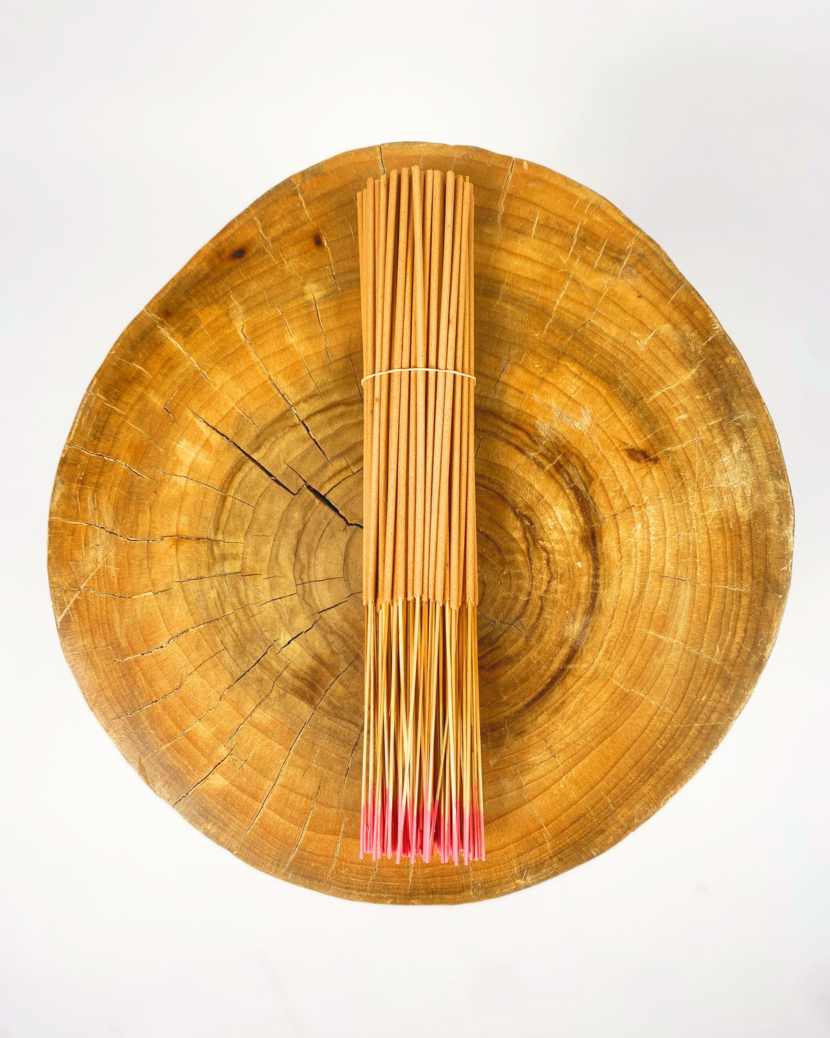 Incense sticks bundle on round wooden tray, light tan with pink tips