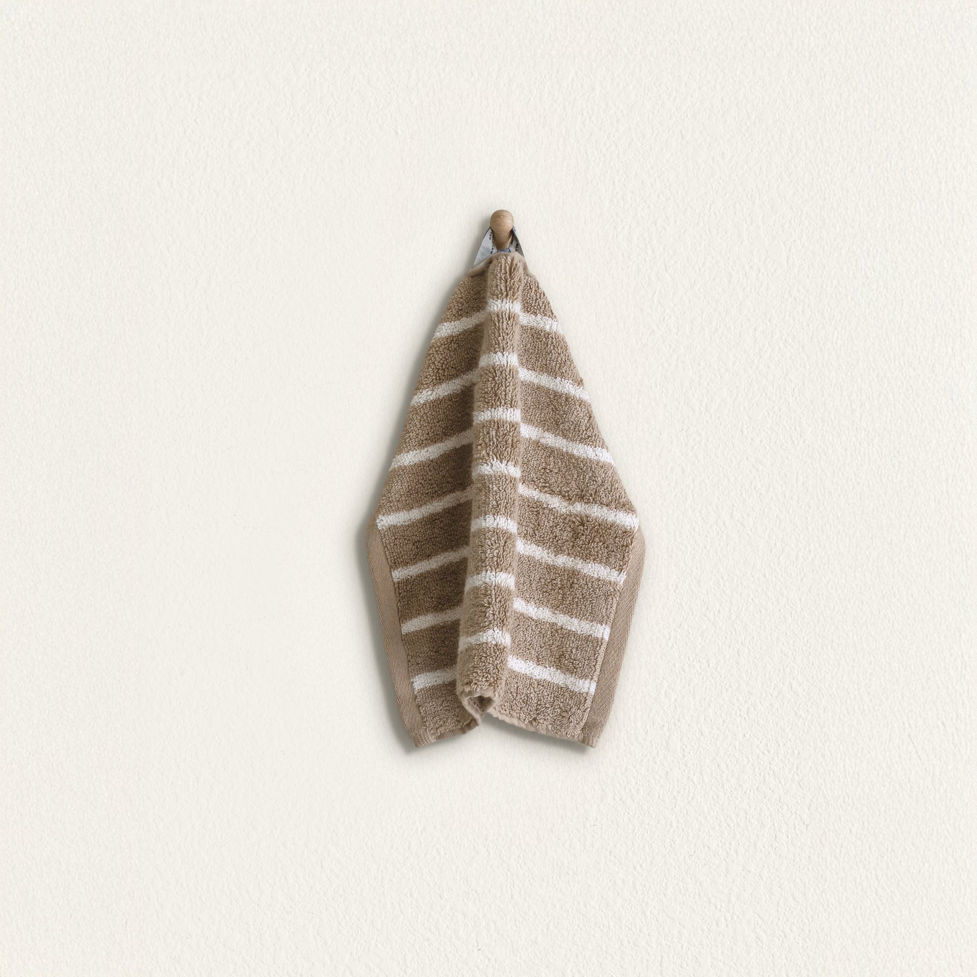 Striped cotton hand towel hanging, taupe with white stripes and folded terry texture