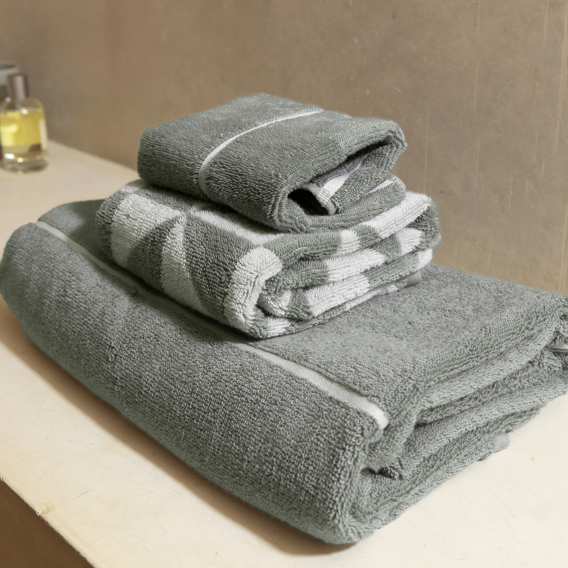 Sage green cotton bath towels, stacked with white striped bands