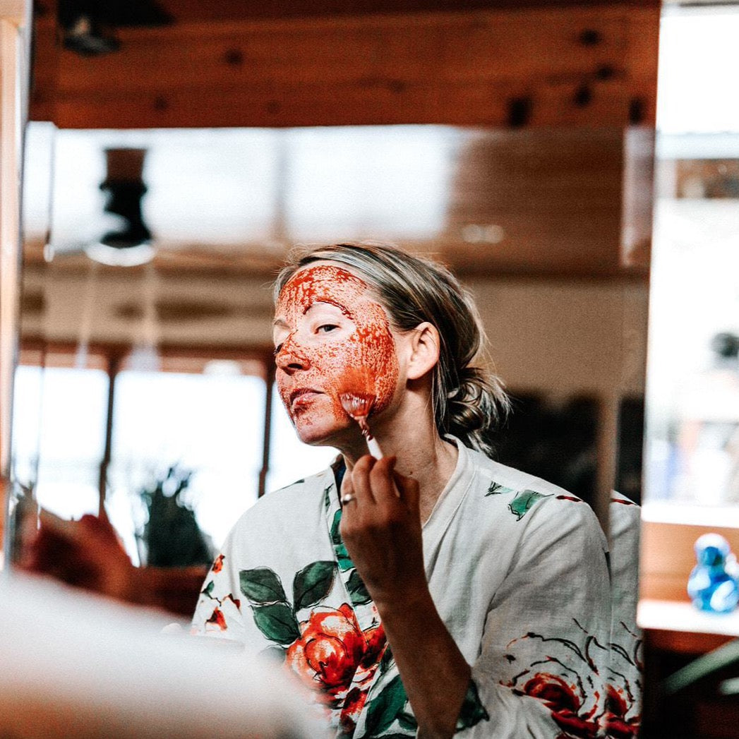 Person wearing red clay face mask, hand applying product near chin