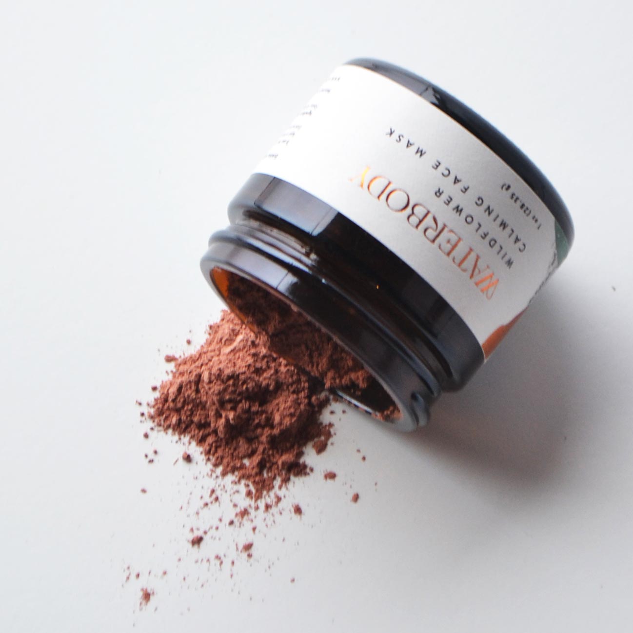 Face mask jar with dark lid and clay powder spill beside it