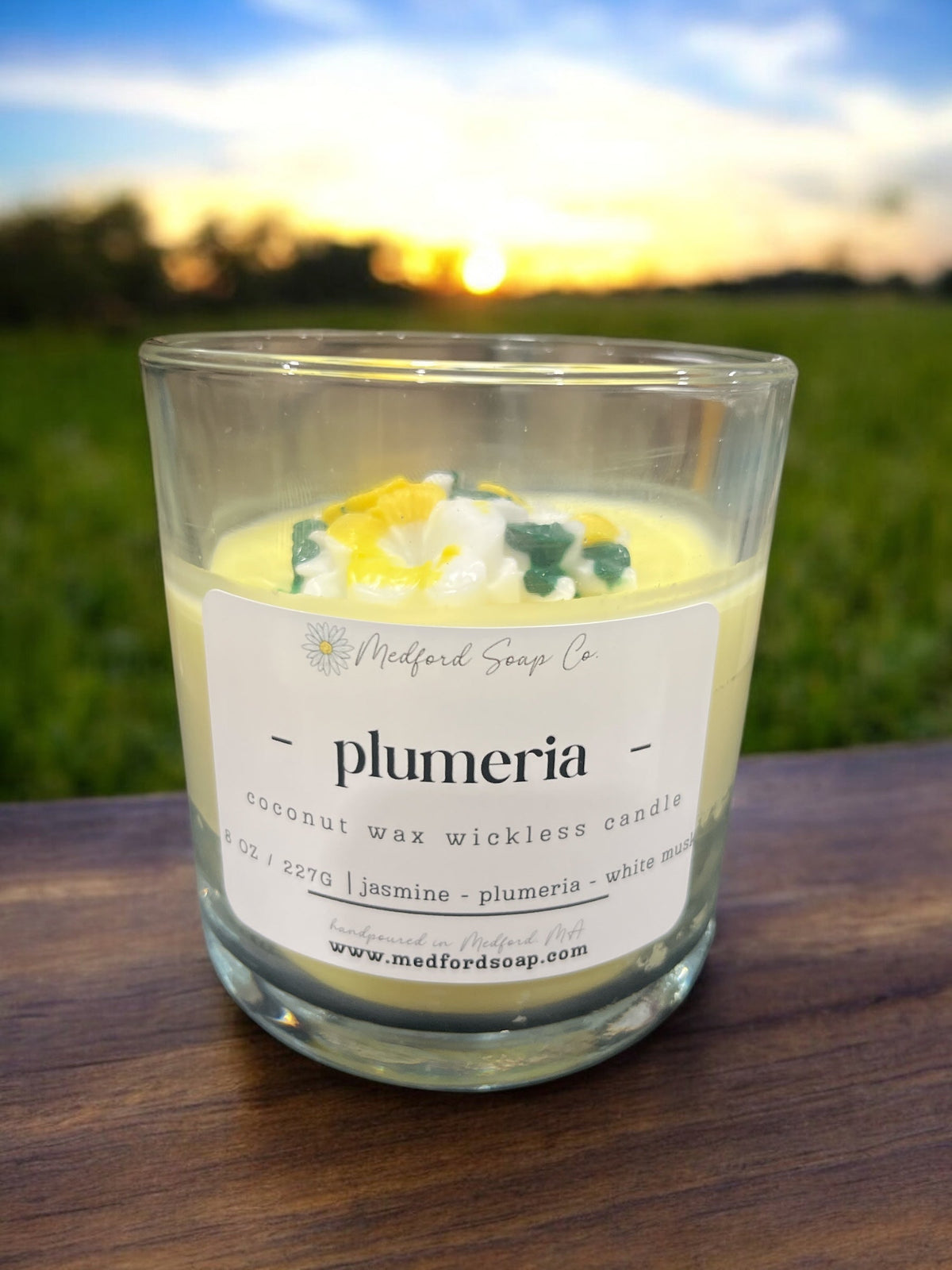 Wickless candle in clear glass jar with “plumeria” label and yellow wax with colored accents