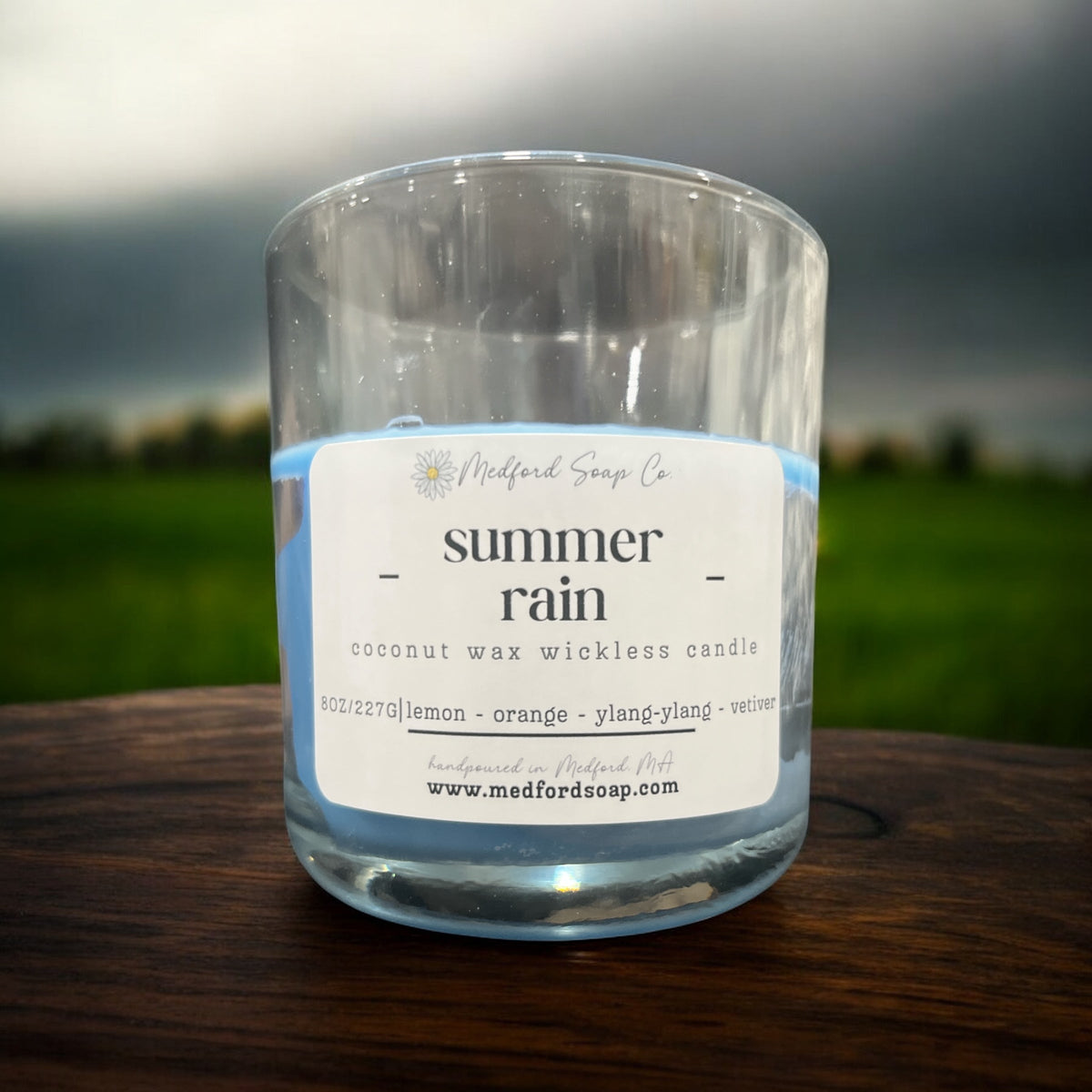 Wickless candle in clear glass jar with “summer rain” label and pale blue wax at bottom