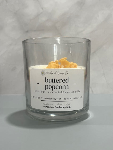 Wickless candle in a clear glass jar with buttered popcorn wax label
