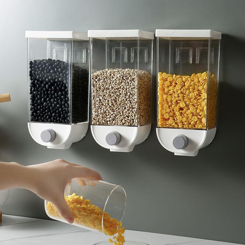 Wall-mounted kitchen sealed grain jars, three clear bins; hand pours yellow kernels