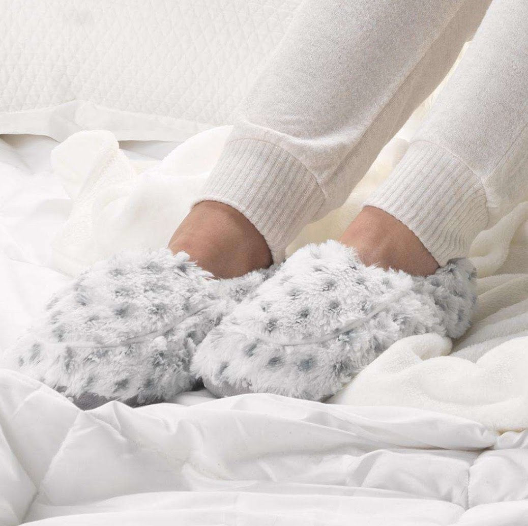 White plush slippers with light blue dotted pattern worn on feet over white fabric