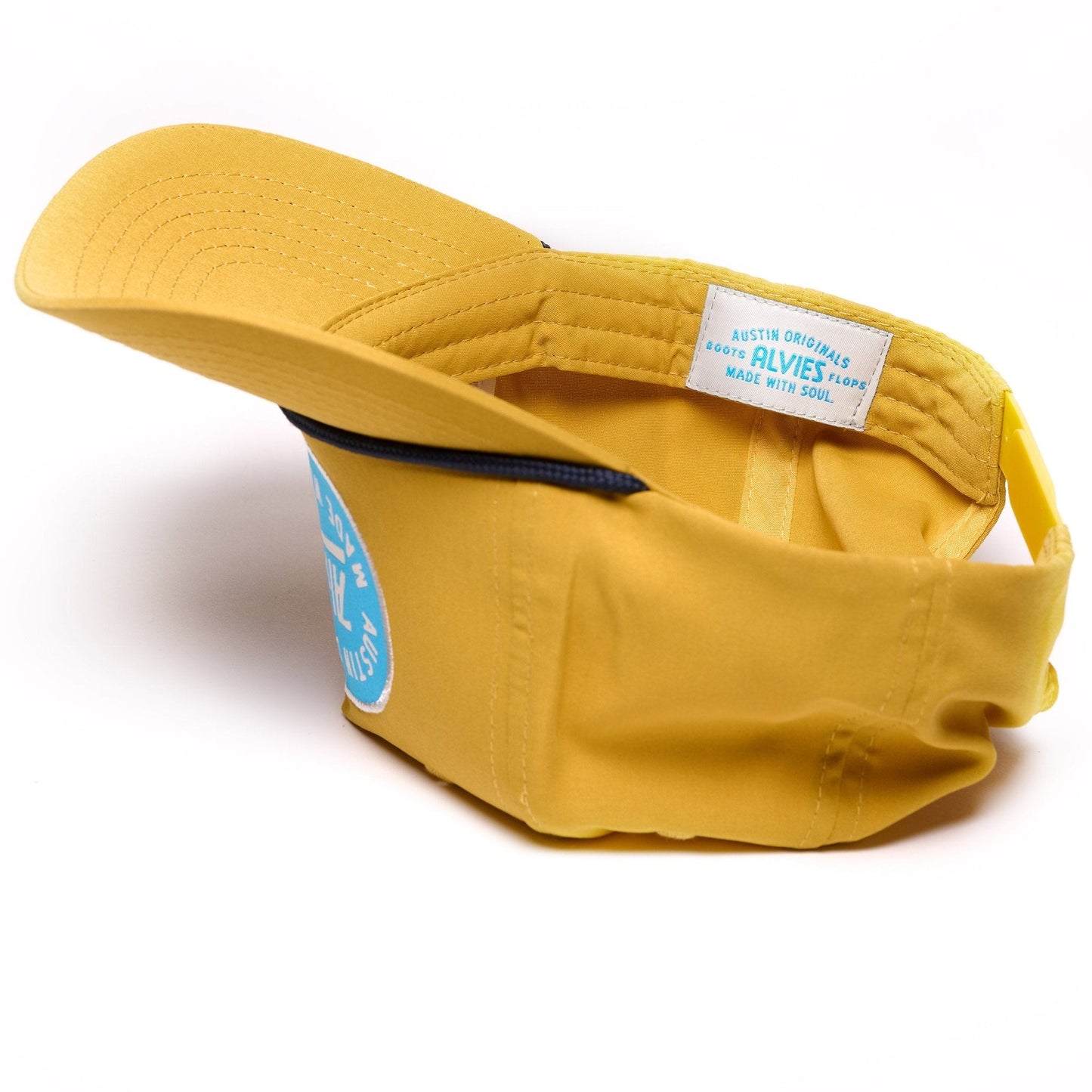 Yellow snapback hat, side view with blue logo patch and fabric strap detail.