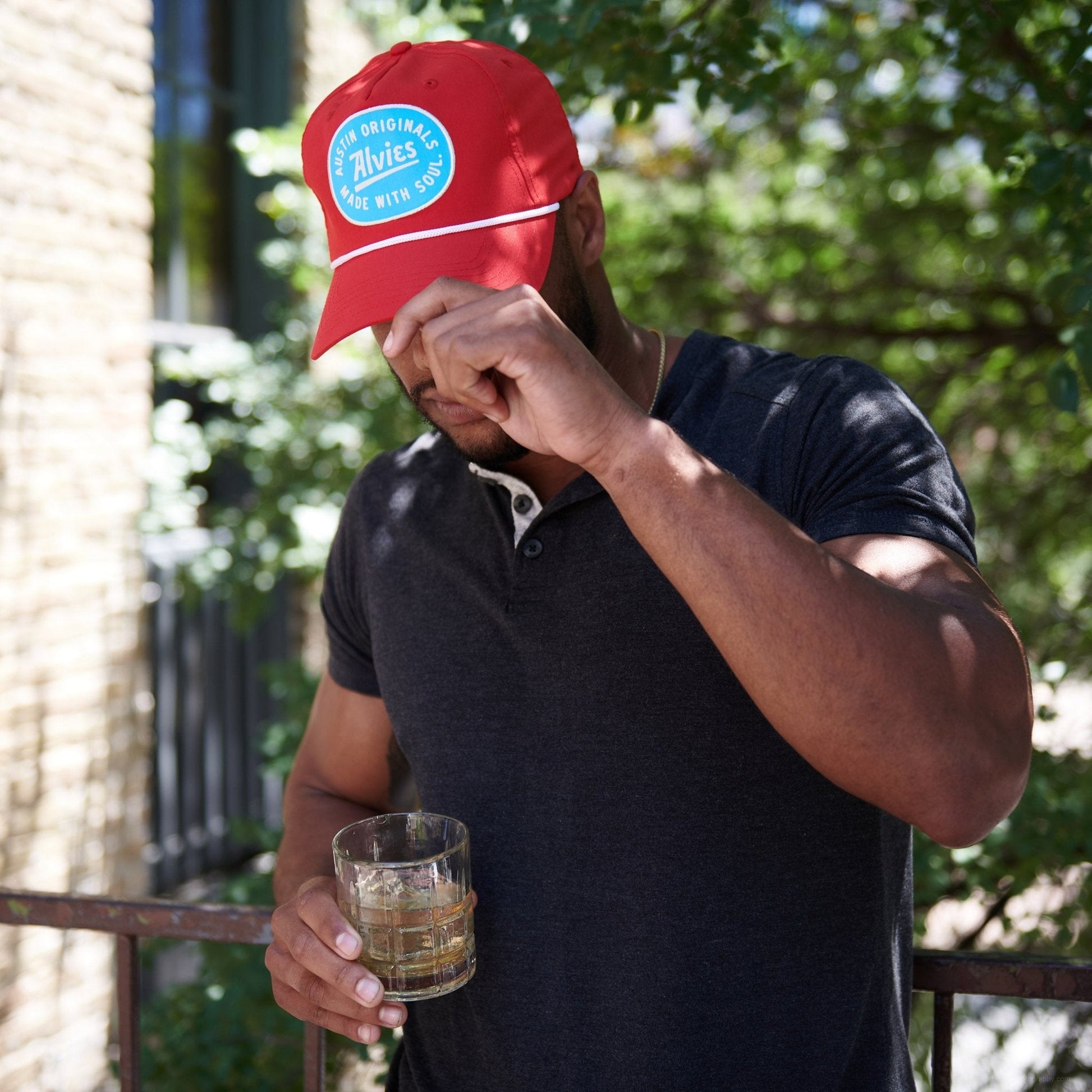 Red snapback hat on a person, featuring a blue oval logo patch on the front.