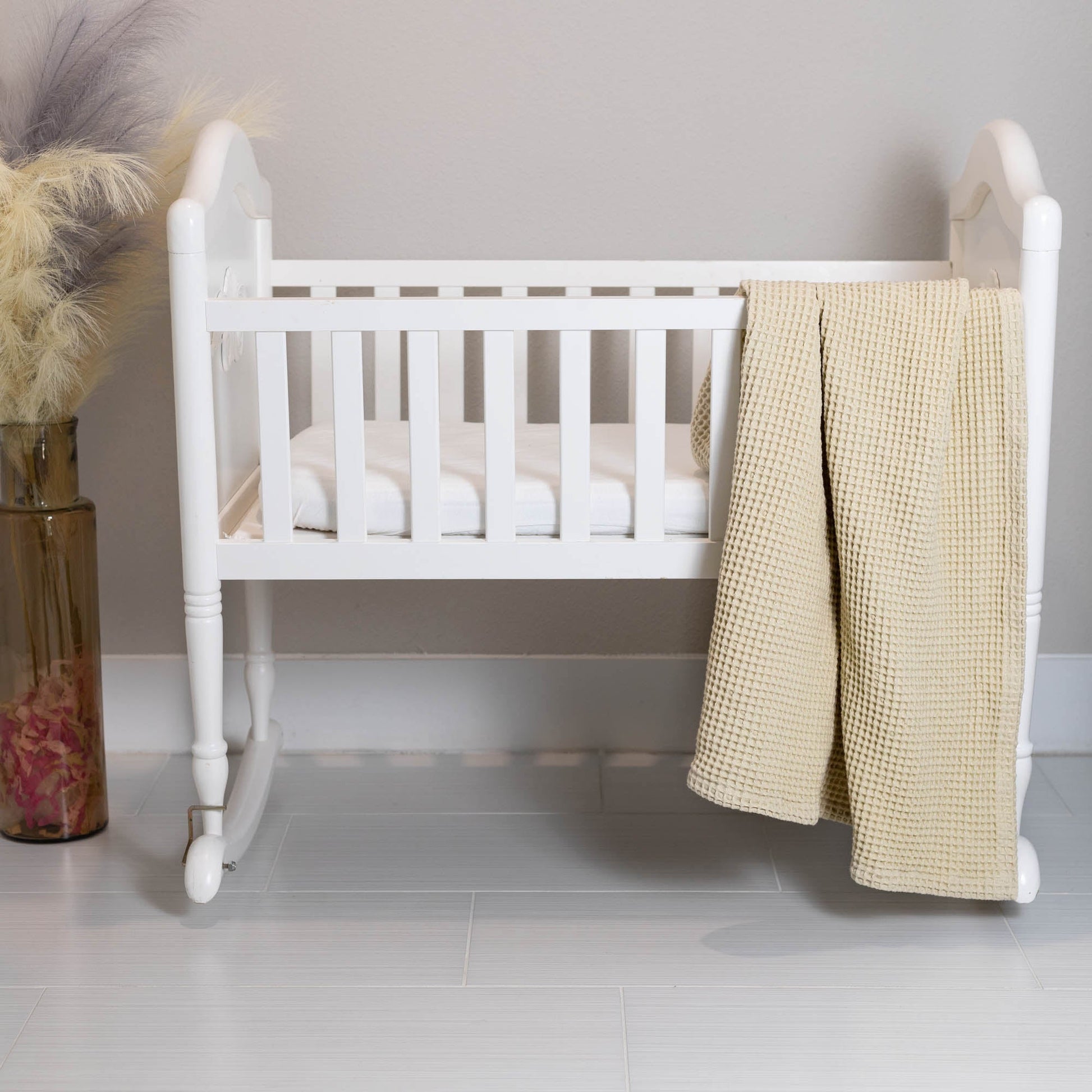 Waffle baby blanket in ivory, hanging over a crib side in waffle texture