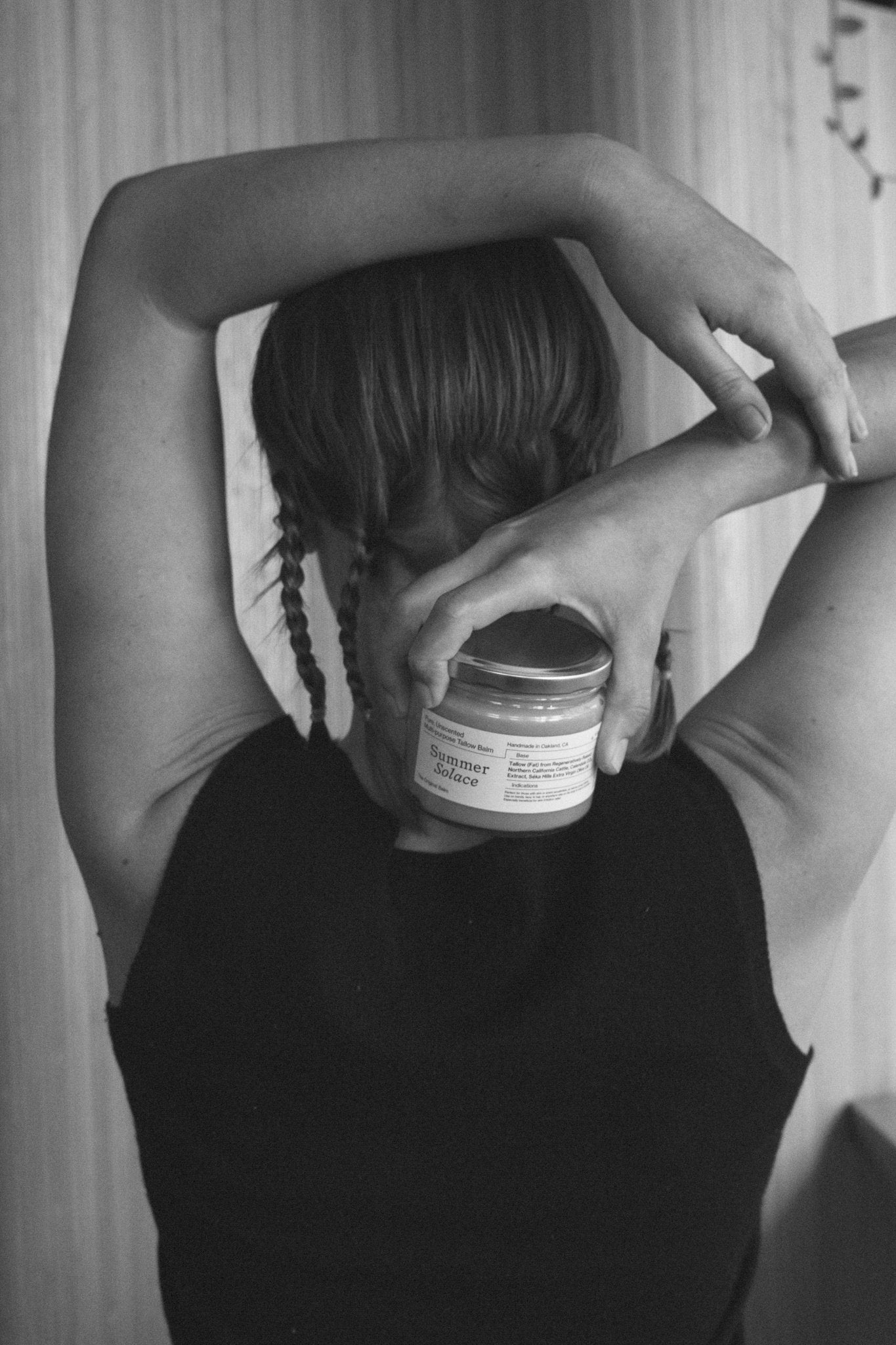 Woman holding a balm jar to her face with both hands, dark hair visible
