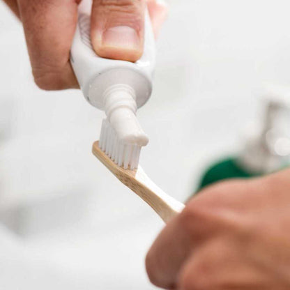 Bamboo toothbrush in hand with white bristles and light wood handle