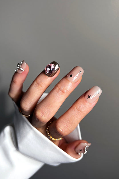 Hand wearing nude gel nails with rhinestone trim and gold-and-silver gem accents