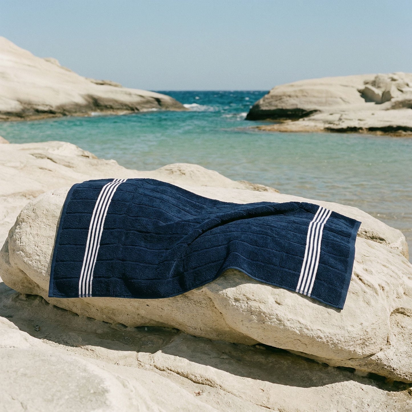 Navy cotton towel with white striped bands laid on a rock
