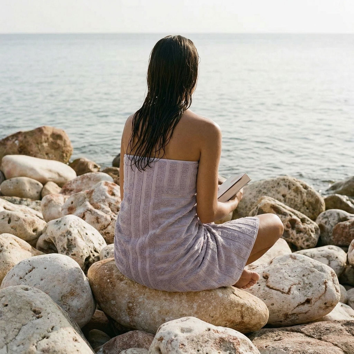 Lilac cotton towel wrap-style, draped over an adult seated on rocks.