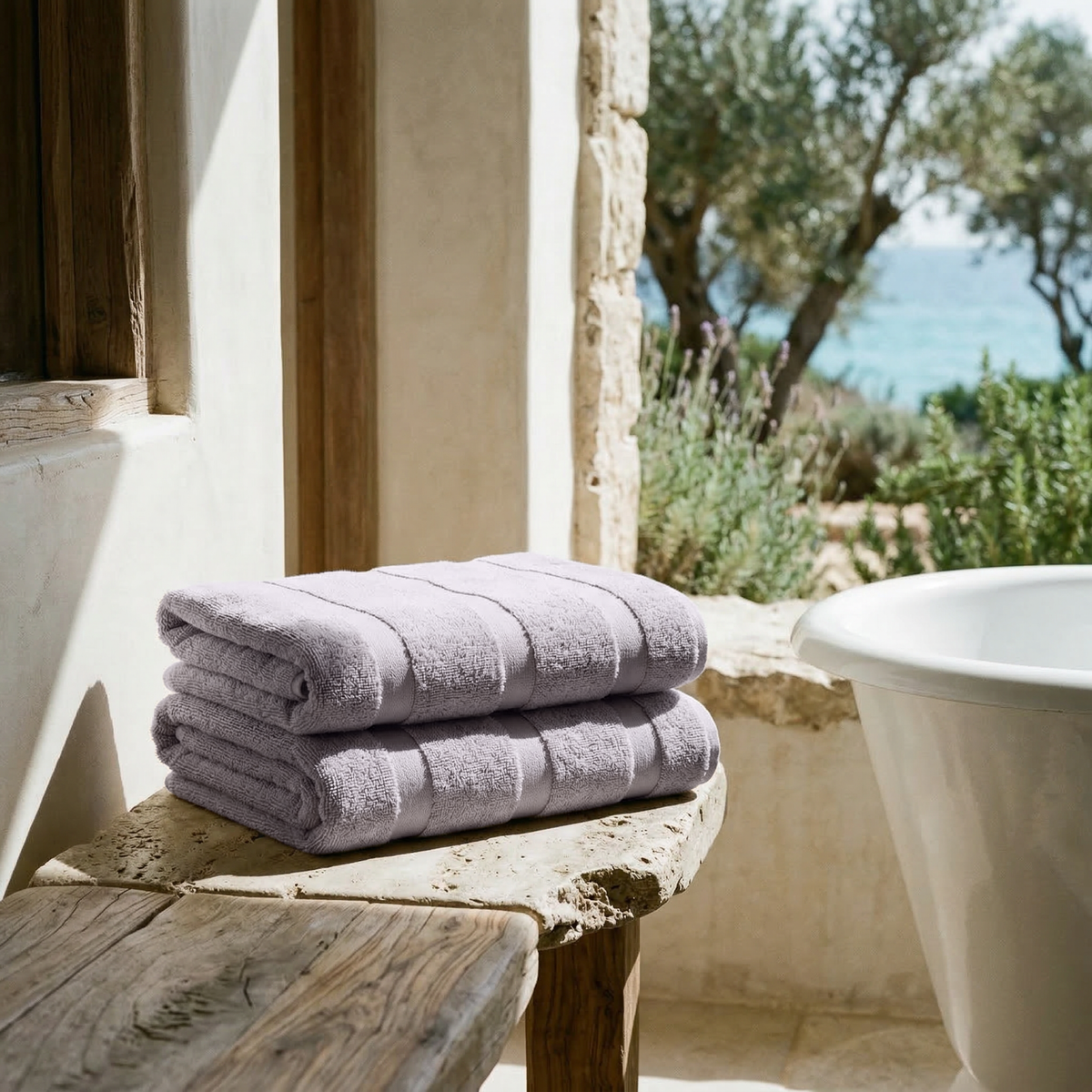 Lilac cotton towel stack with multiple folds, placed on a ledge near a bathtub.