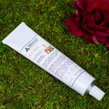 Hand lotion tube lying on grass, white tube with BRIGID BELTANE label
