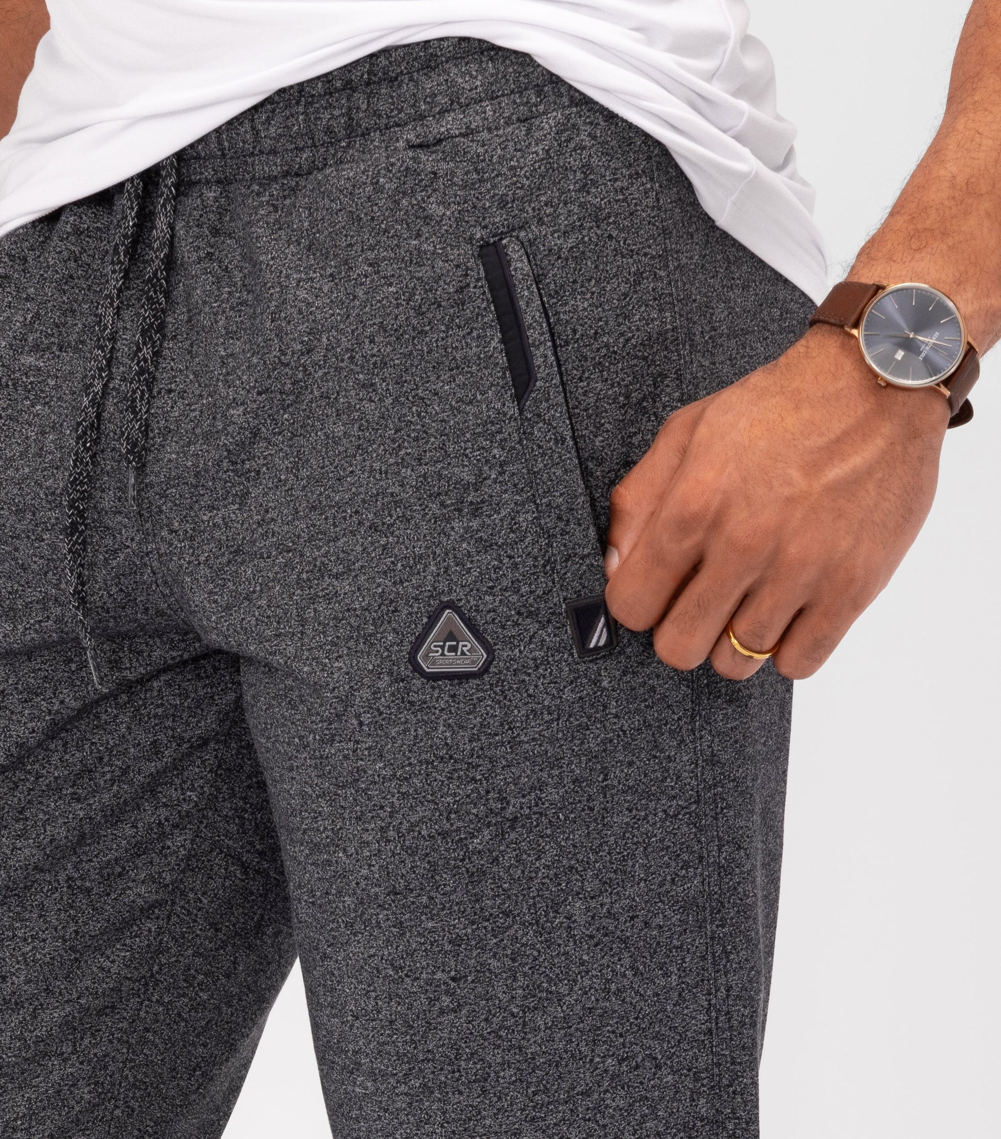Dark charcoal gray athletic sweatpants close-up: elastic waistband, logo patch, side pocket seam.