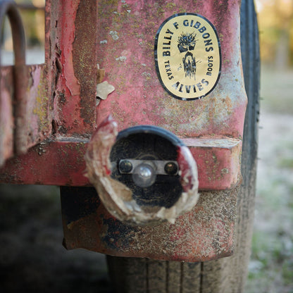 Round sticker with black logo and text on rust-red metal panel