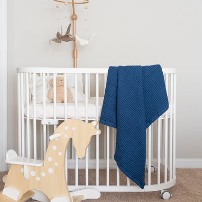 Waffle baby blanket in blue, draped over a white crib rail