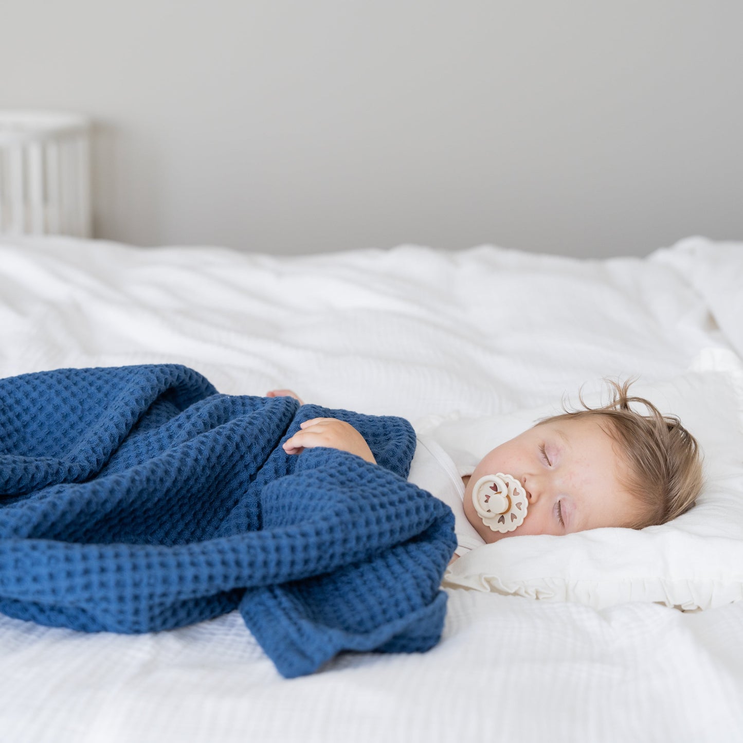 Waffle baby blanket in blue, folded and draped over a sleeping baby