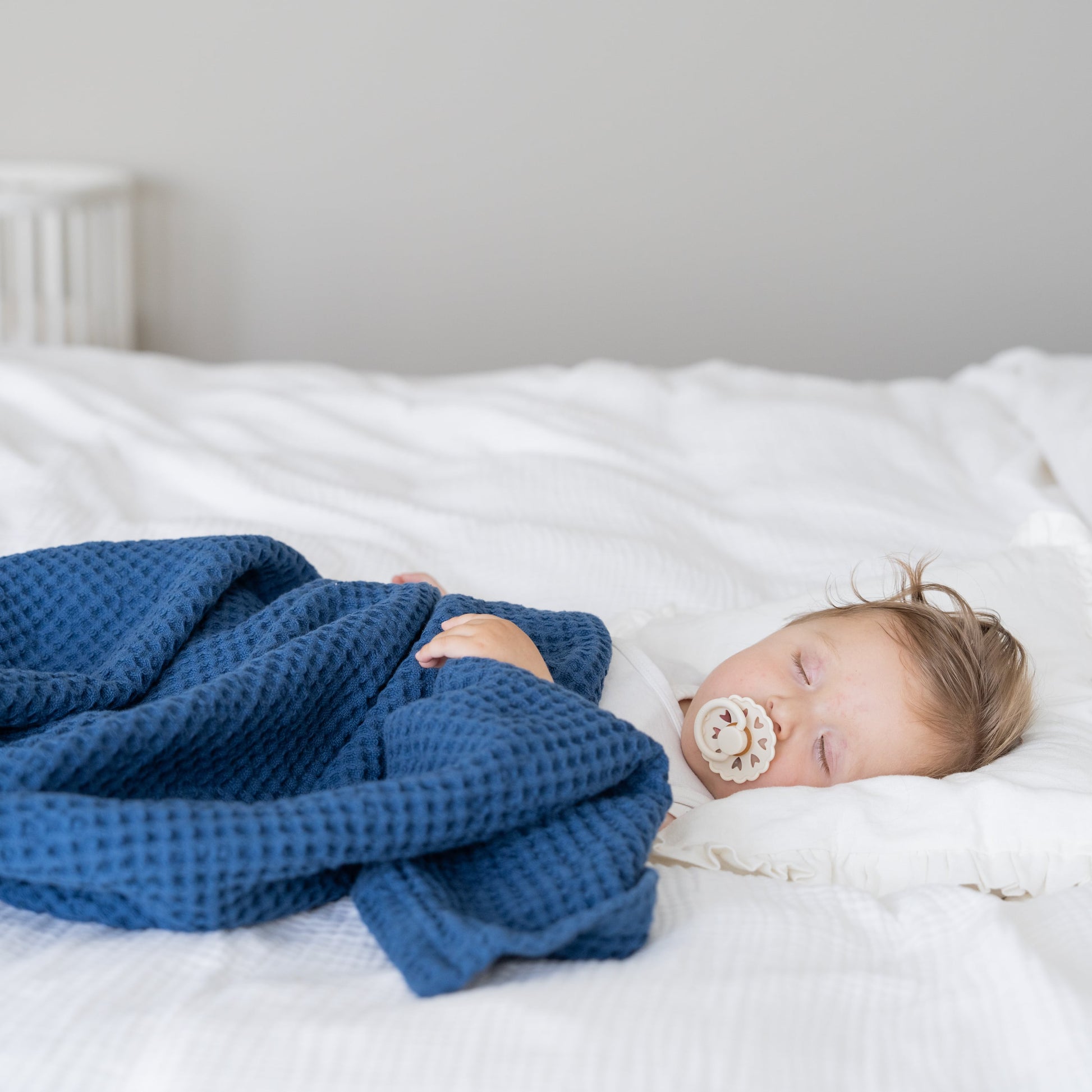 Waffle baby blanket in blue, folded and draped over a sleeping baby
