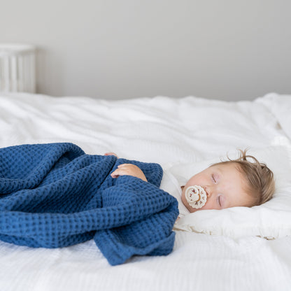 Waffle baby blanket in blue, folded and draped over a sleeping baby