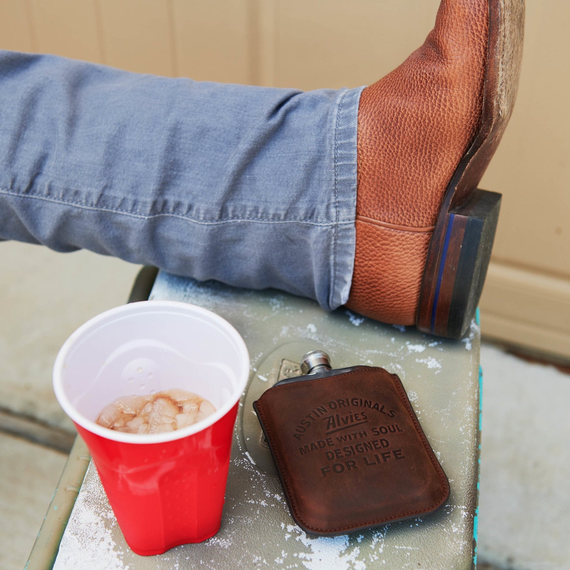 Brown boot flask with engraved face placed on an ice-covered surface.