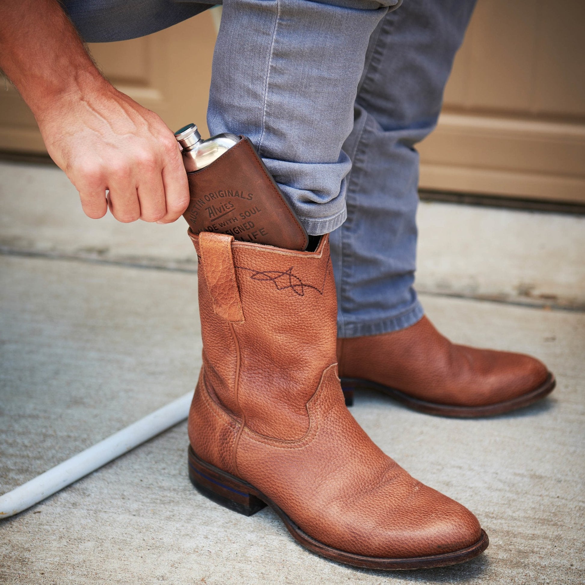 Brown leather boot flask tucked into a boot, with silver spout visible.