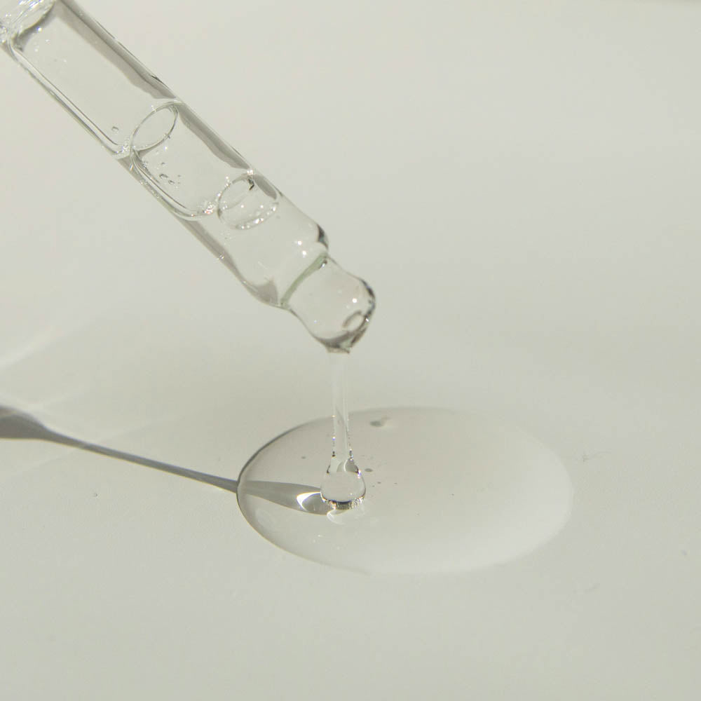 Glass dropper pouring clear liquid onto a white surface