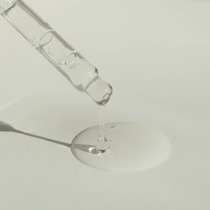 Glass dropper pouring clear oil into a white dish