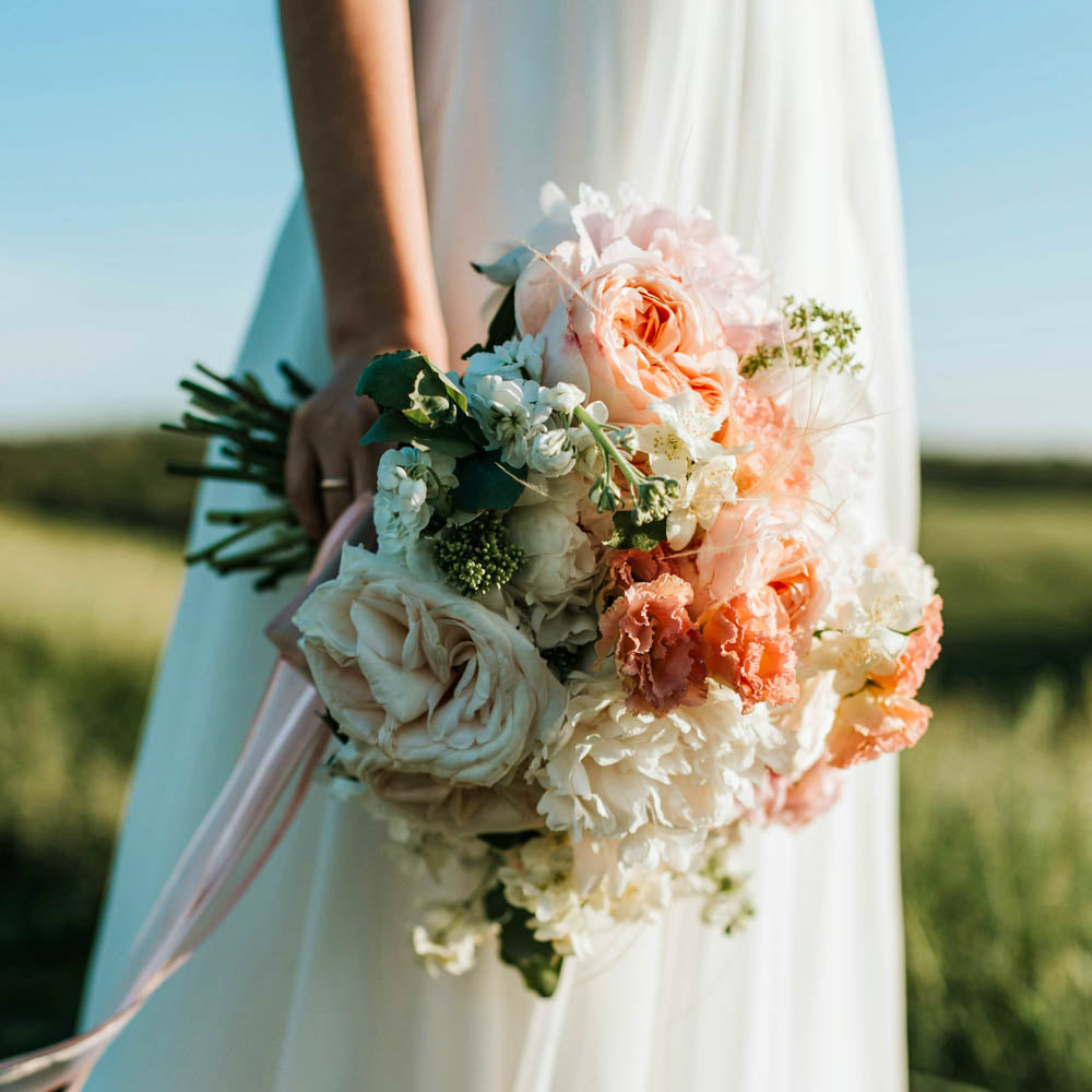 Floral bridal bouquet with peach and white flowers, held against a white dress