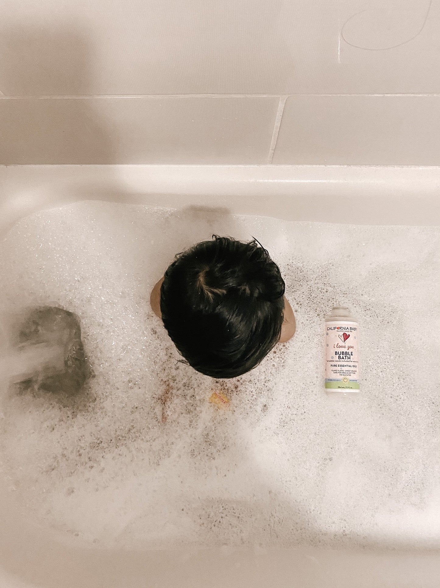 Bubble bath bottle in bathtub foam, pink liquid, label facing up