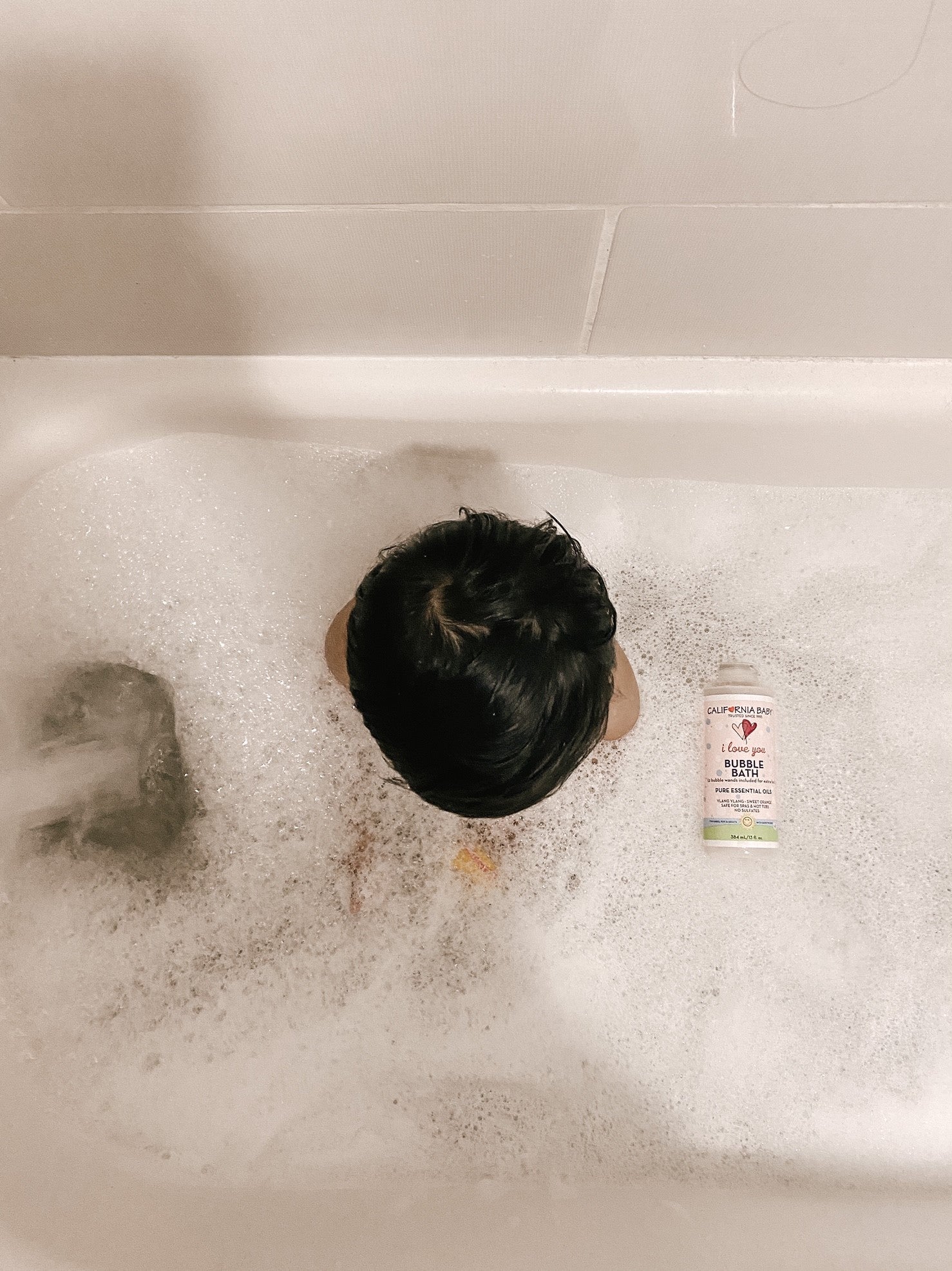 Bubble bath bottle in bathtub foam, pink liquid, label facing up