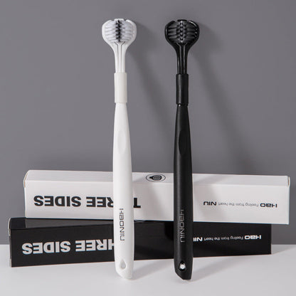 Triple-sided soft bristle toothbrushes, white and black, with packaging behind