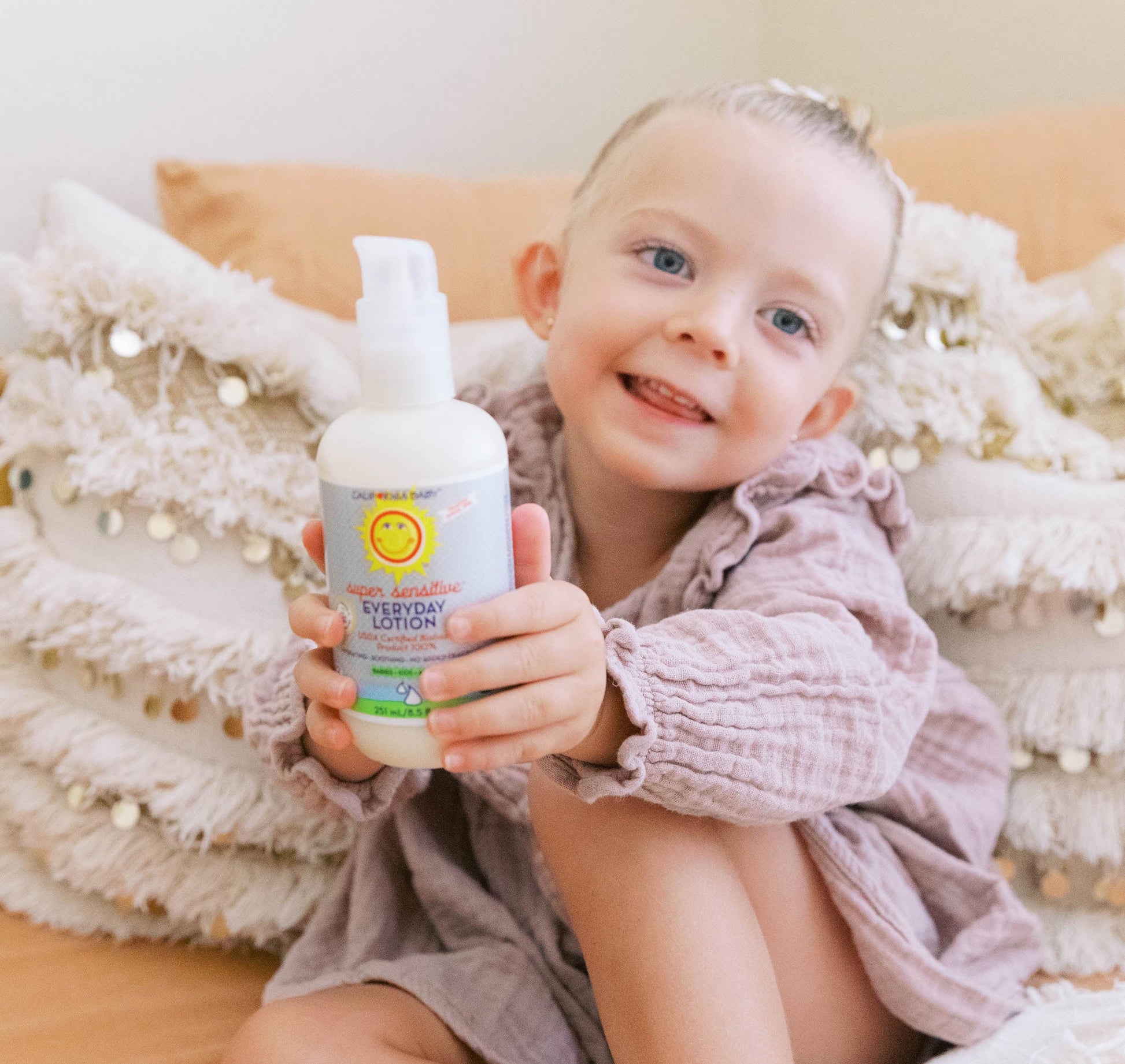 Fragrance-free everyday lotion bottle with pump held beside a smiling baby