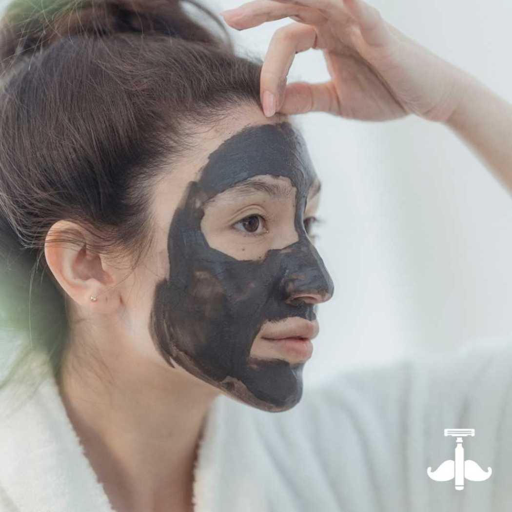 Dark gray clay mask on face, hand smoothing