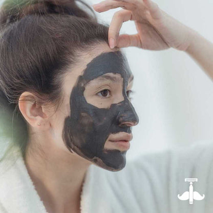 Dark gray clay mask on face, hand smoothing