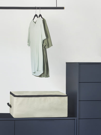 Comforter storage bag on cabinet top, beige with black trim and top zipper