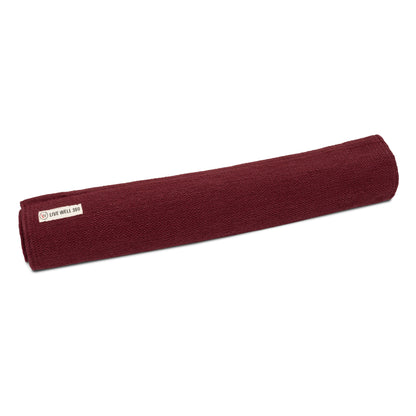 Organic cotton yoga mat, maroon rolled with fabric label at side.