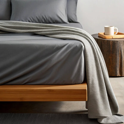 Graphite gray sheet set with draped gray throw blanket on a bed.