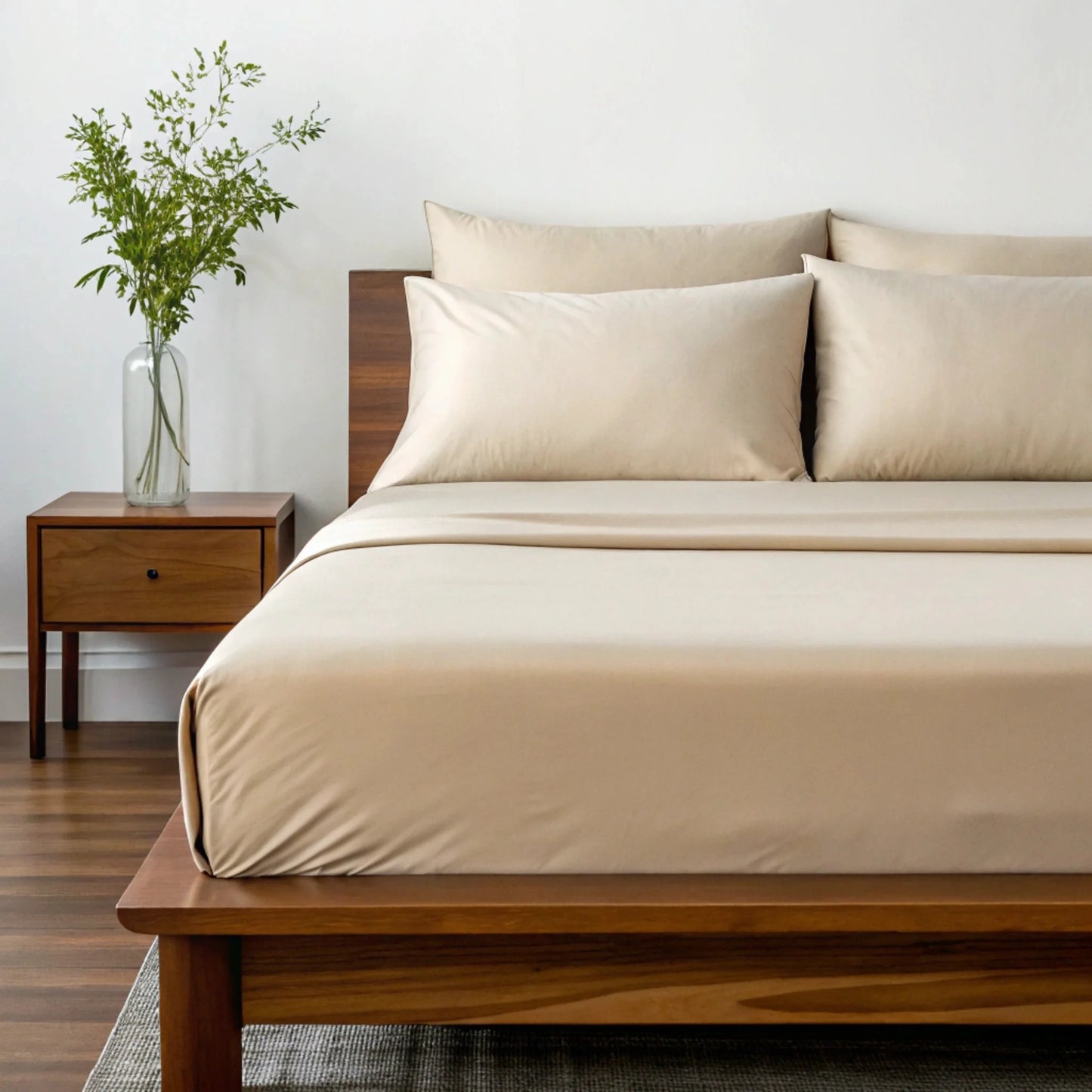 Beige sheet set with two pillows and duvet cover on wooden bed frame.