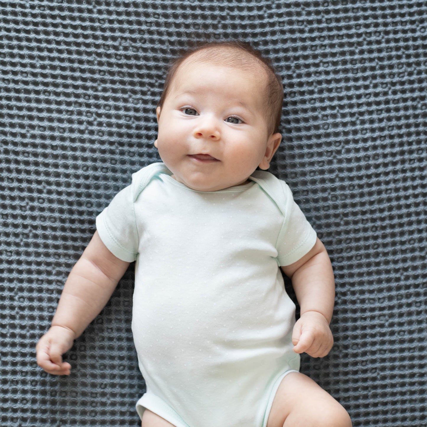 Waffle baby blanket in dark gray, waffle weave background behind a baby