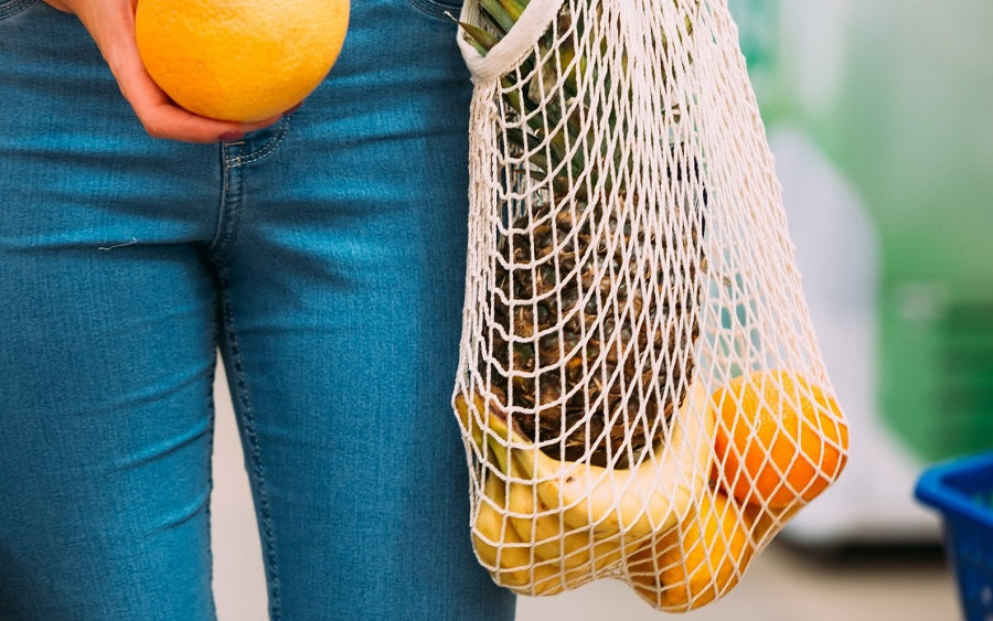 Mesh net bag with long straps, holding oranges and yellow items near jeans