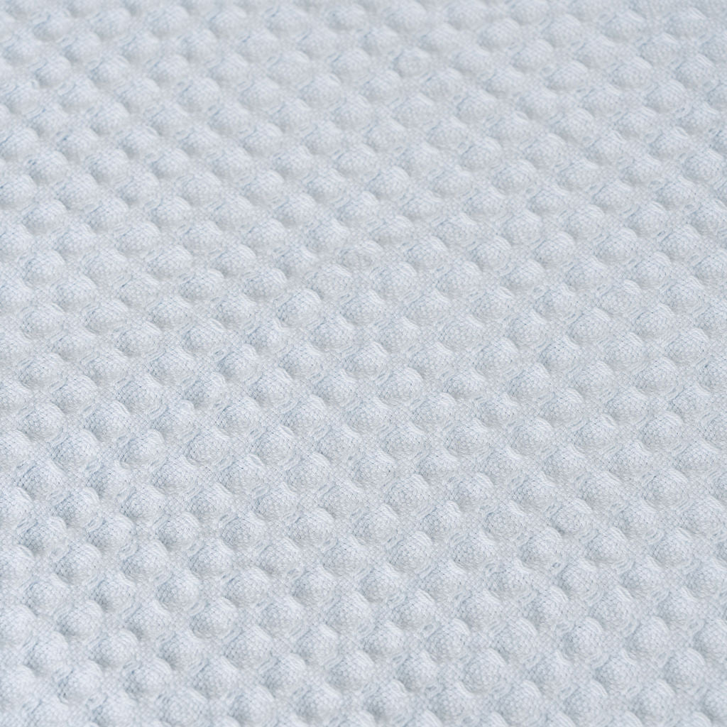 Close-up of light blue waffle weave fabric texture with small raised squares.